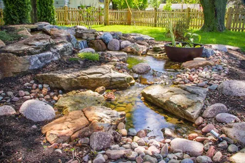 A Patio Pond with aquatic plants was cleverly added to the edge of this waterfall's stream.