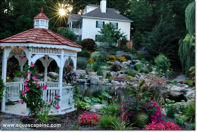 A cottage-style gazebo provides the optimal viewing vantage of this lovely pond and waterfall.