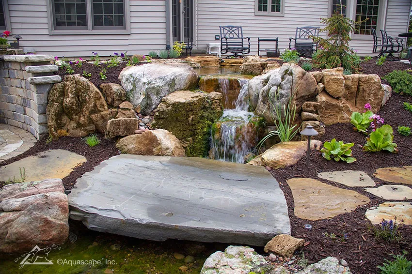 A stone bridge in this backyard creates a place to sit and dangle your feet in the water.